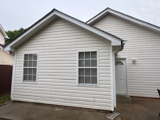 Back of a home with white siding, windows, door, and concrete patio.