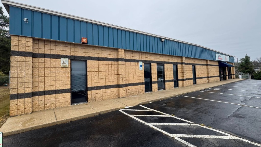 Long one-story commercial building with block facade, metal siding, and parking lot.